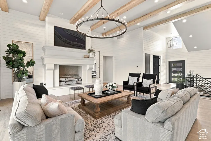 Vaulted ceiling with wood beams, shiplap walls, wood-finish flooring, a large fireplace with a substantial mantel, and a multi-pane glass entry door