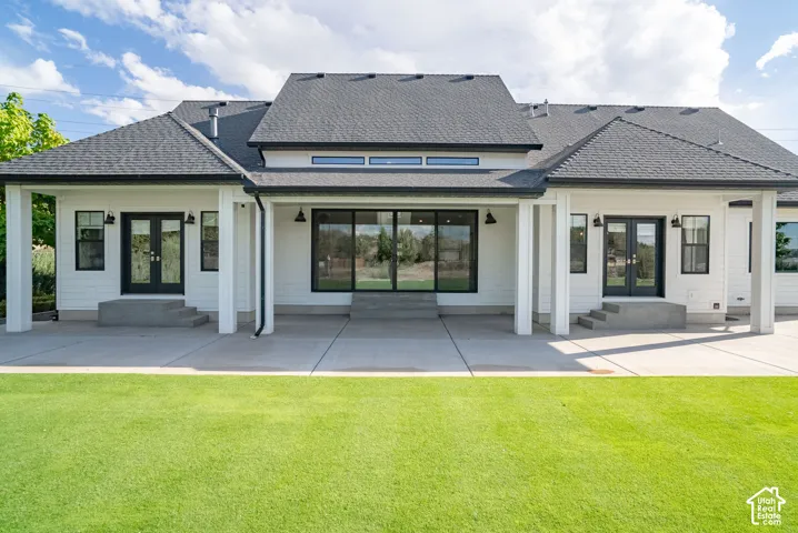 White exterior siding, dark roof, expansive concrete patio, multiple black-framed glass doors, and recessed lighting