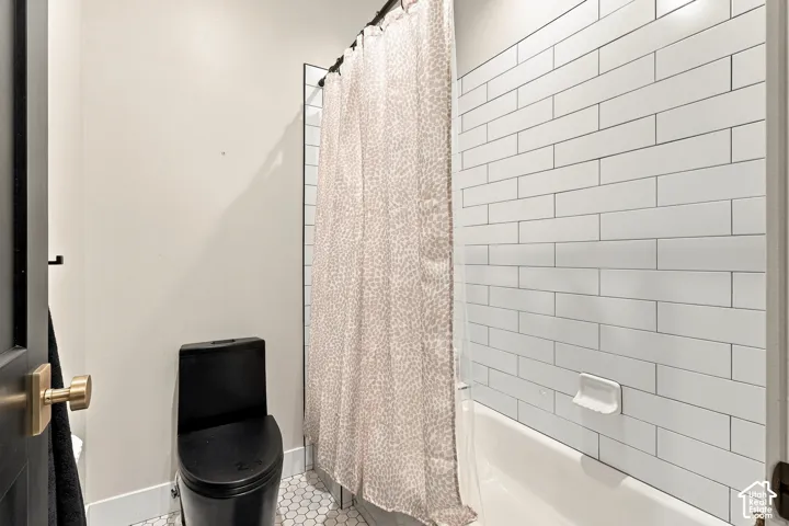White subway tile shower surround with integrated tub, black toilet, and hexagonal floor tiles