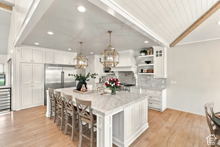 Spacious kitchen featuring an expansive central island with stone countertop, white cabinetry, wood-finish flooring, recessed lighting, and decorative pendant fixtures