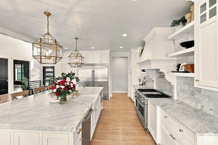 Gourmet kitchen featuring a large island with white stone countertops, white shaker cabinetry, stainless steel appliances, and wood-finish flooring