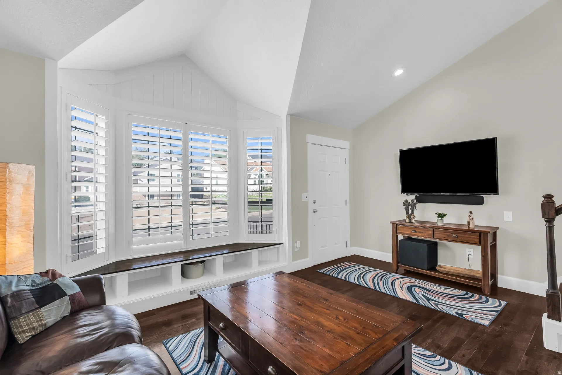 Bay window with plantation shutters, vaulted ceiling, recessed lighting, wood-finish flooring, and a white entry door