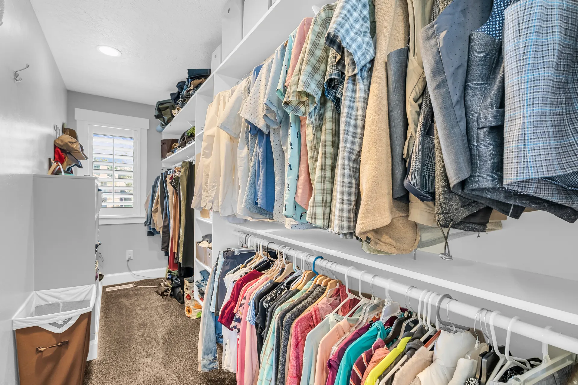 Walk-in closet featuring extensive built-in shelving, multiple hanging rods, and a window with plantation shutters