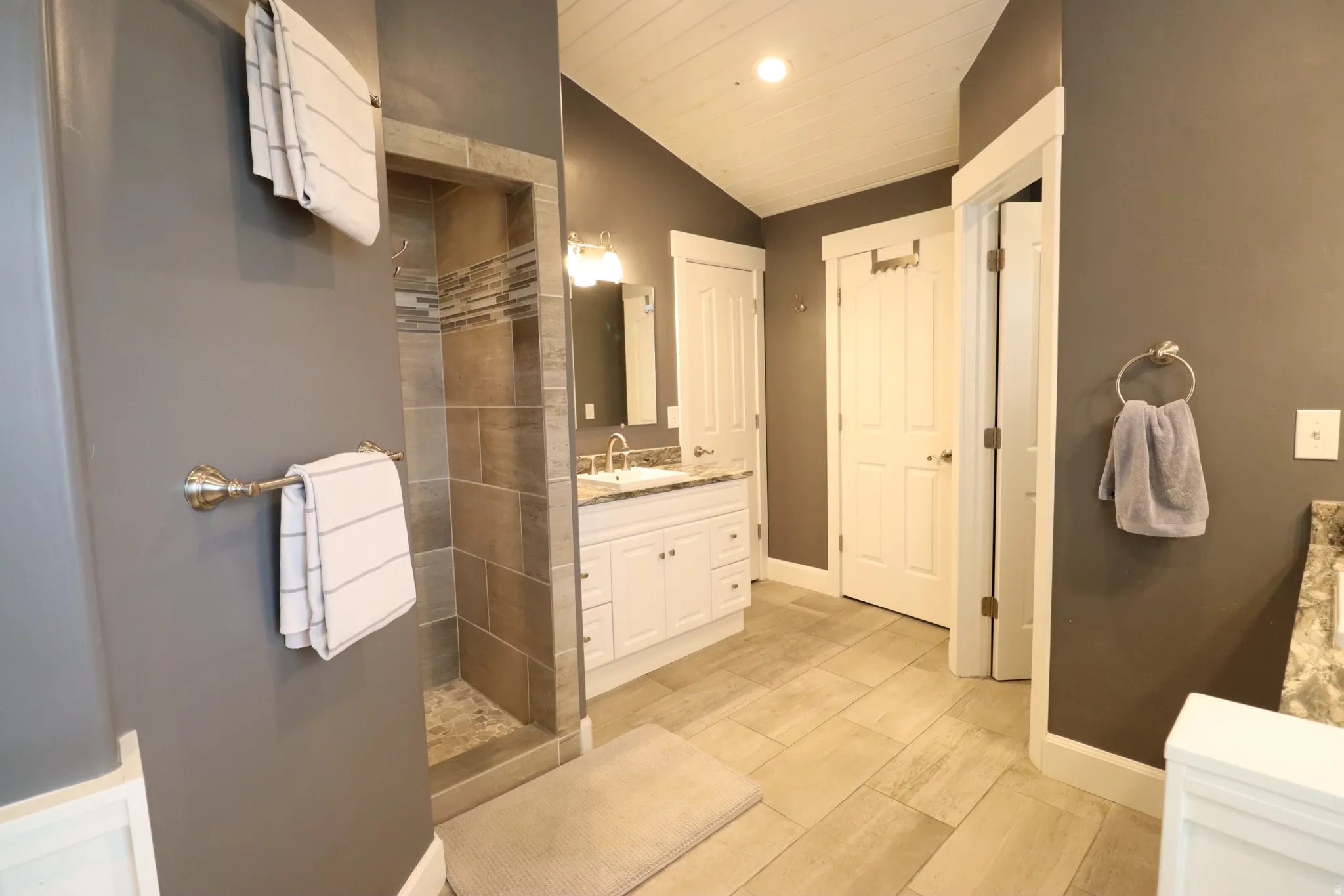 Tiled shower stall with mosaic accent wall, with doorless entry.