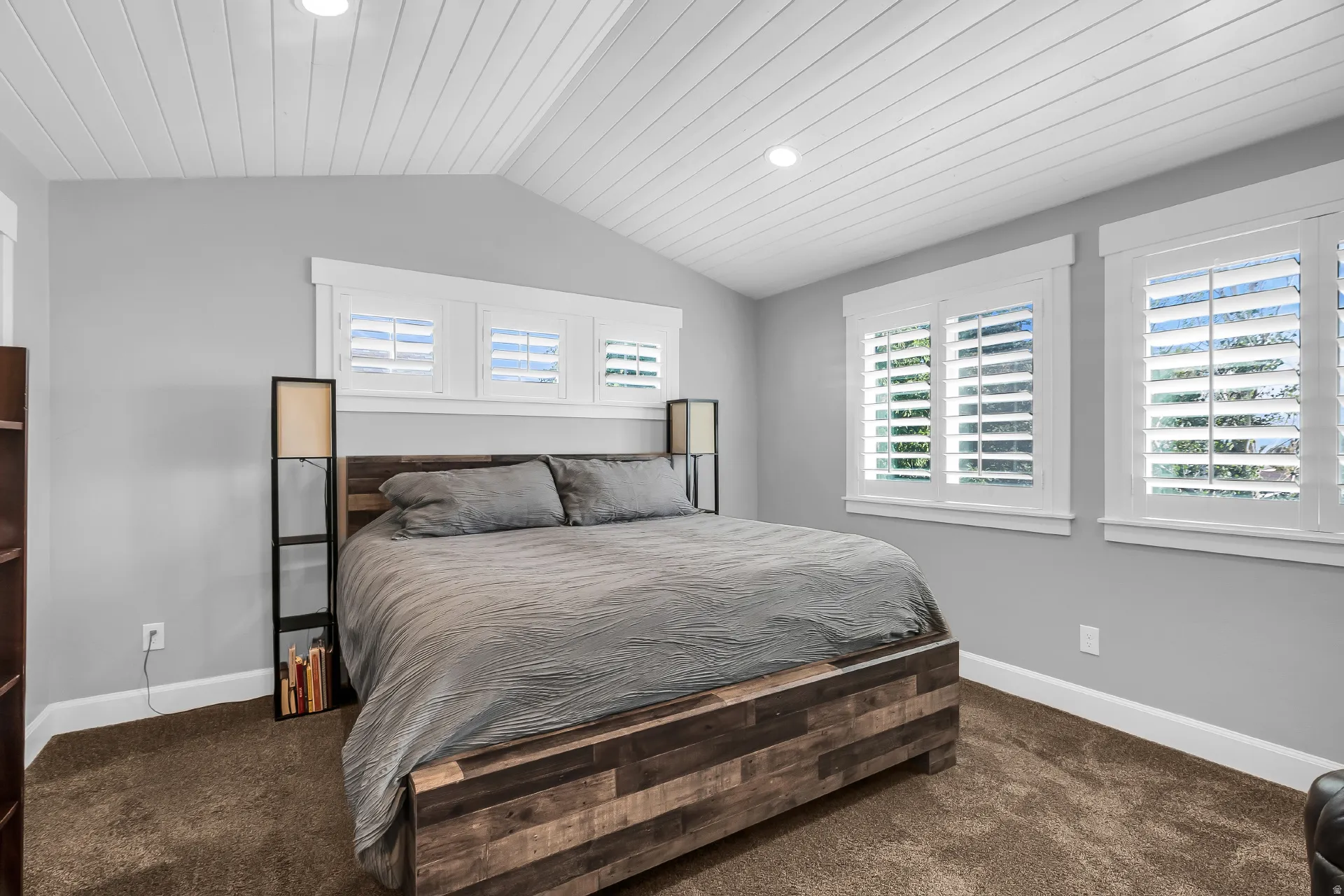Primary bedroom.  Vaulted plank ceiling, recessed lighting, plantation shutters, and light gray wall paint