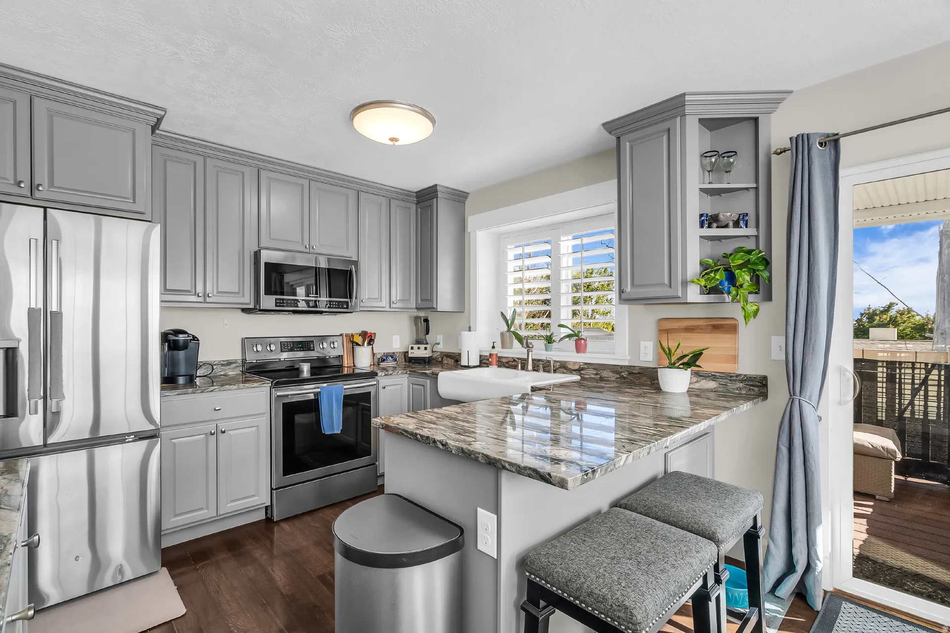 Contemporary kitchen featuring gray cabinetry, stainless steel appliances, a farmhouse sink, stone countertops, and wood-finish flooring