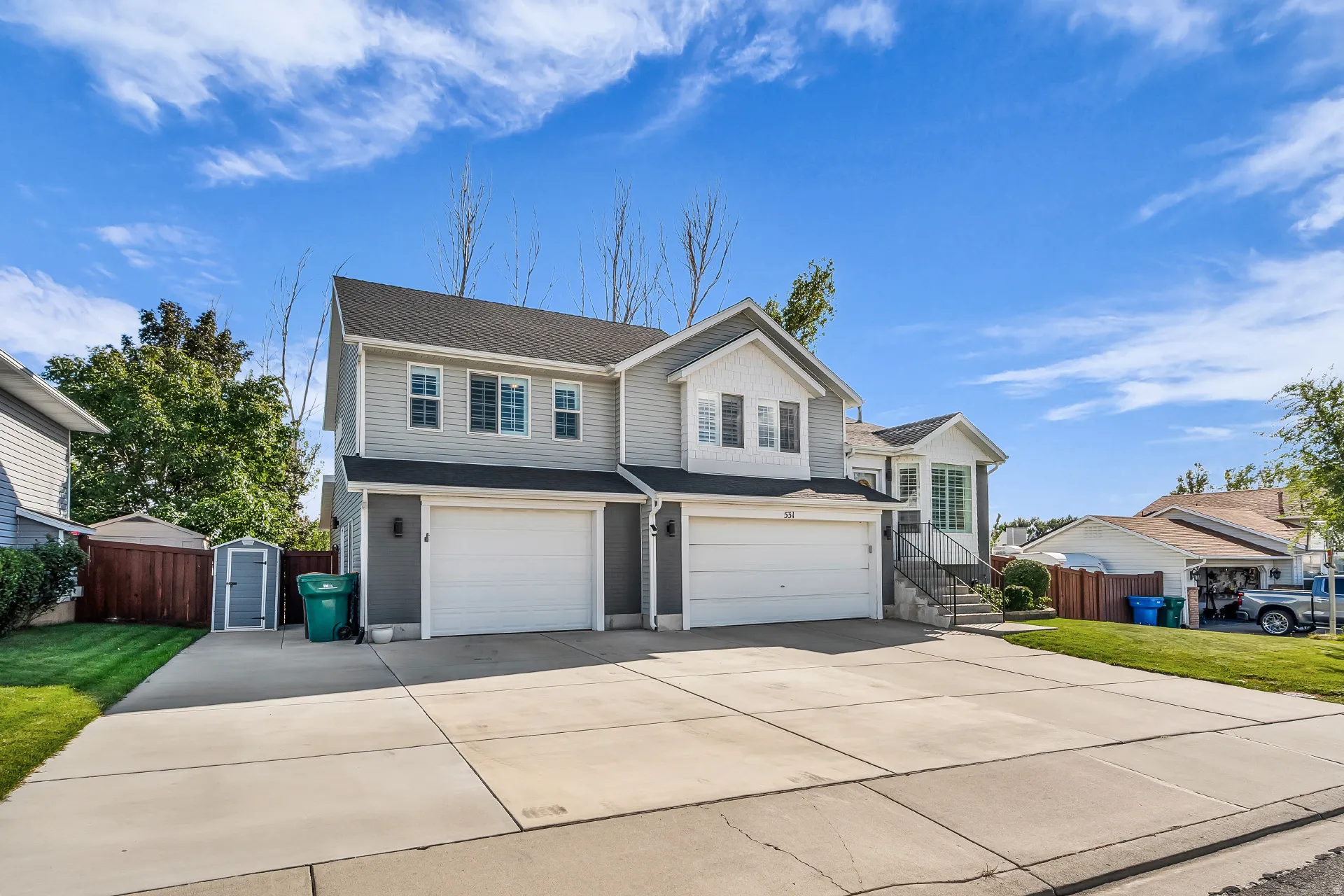 Two-story residence with siding exterior, dual garage doors, concrete driveway, and a fenced yard with a storage shed