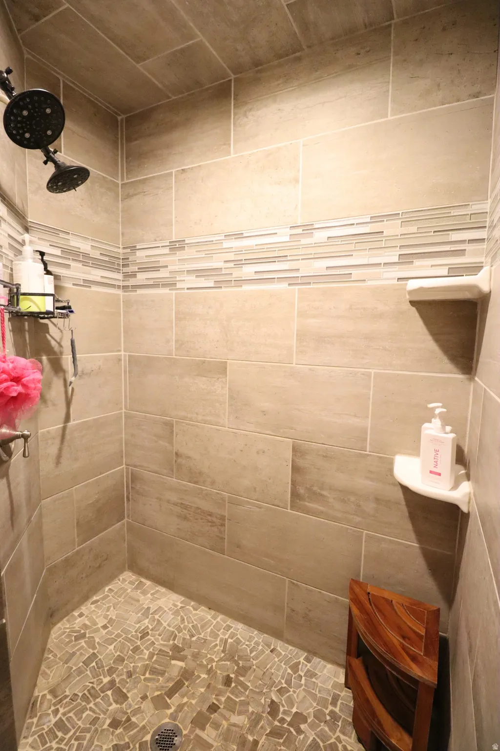 Spacious Primary tiled shower with a decorative mosaic accent band, dual shower heads, and pebble-style floor