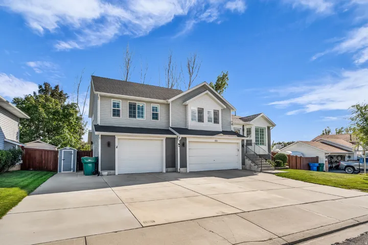 Two-story residence with siding exterior, dual garage doors, concrete driveway, and a fenced yard with a storage shed