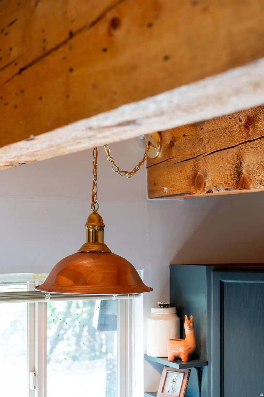 Exposed wood ceiling beams, pendant light fixture with a copper-tone shade, and painted built-in cabinetry