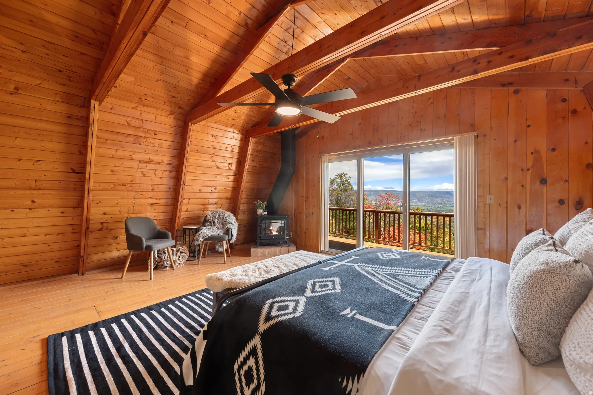 Vaulted wood-paneled ceilings with exposed beams, wood-finish flooring, a built-in wood-burning stove, and sliding glass doors opening to a private balcony