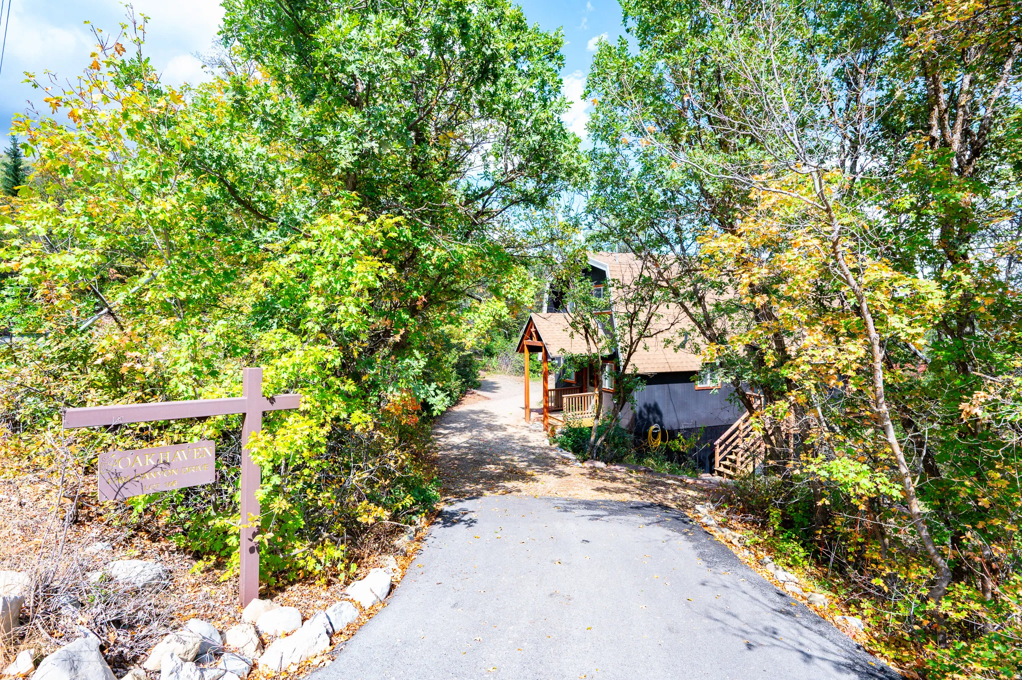 Paved driveway leading to a residence with a covered porch and exterior wood staircase, surrounded by mature trees