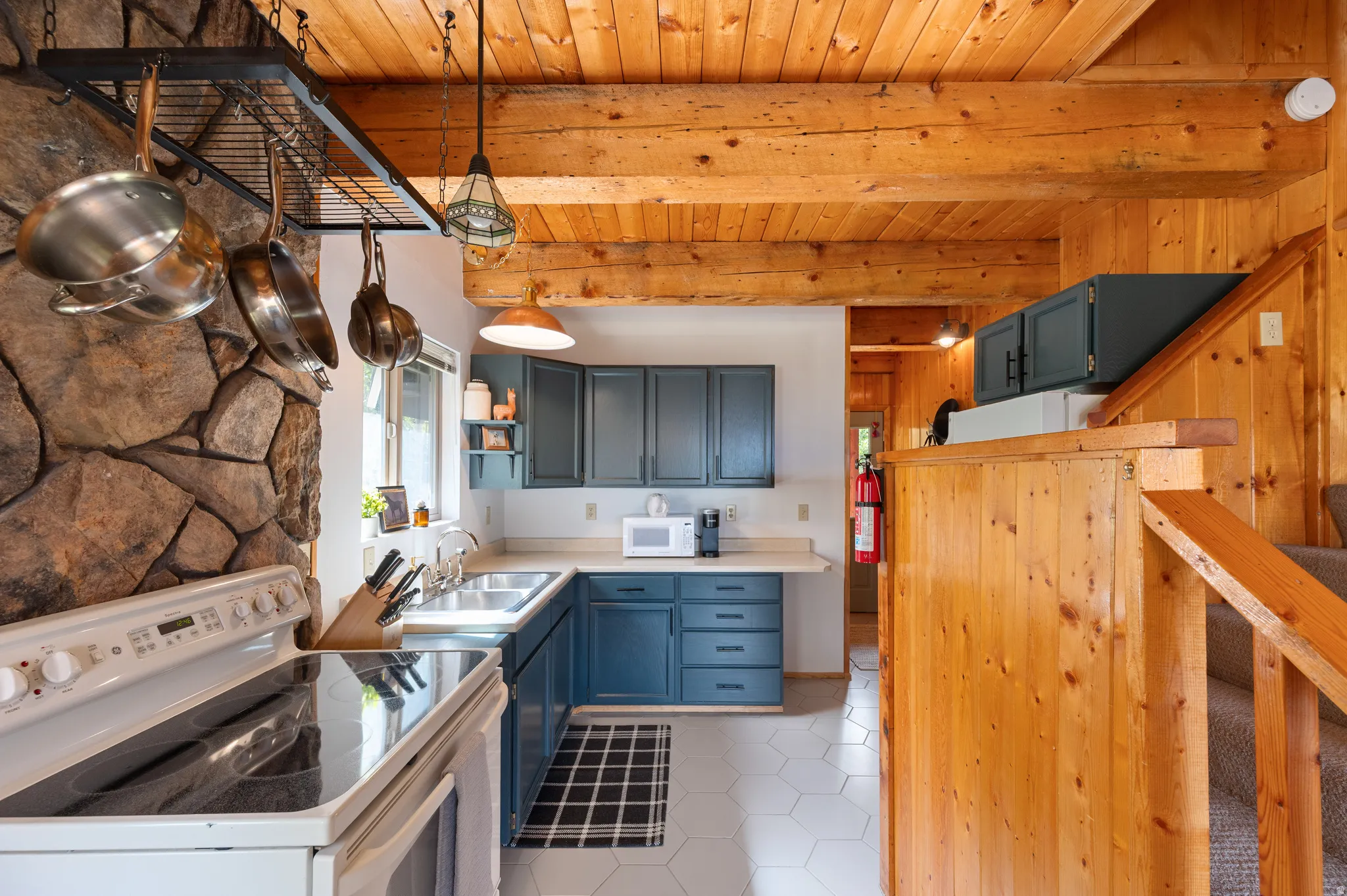 Kitchen featuring a stone accent wall, wood beam ceiling, blue cabinetry, and white hexagonal tile flooring