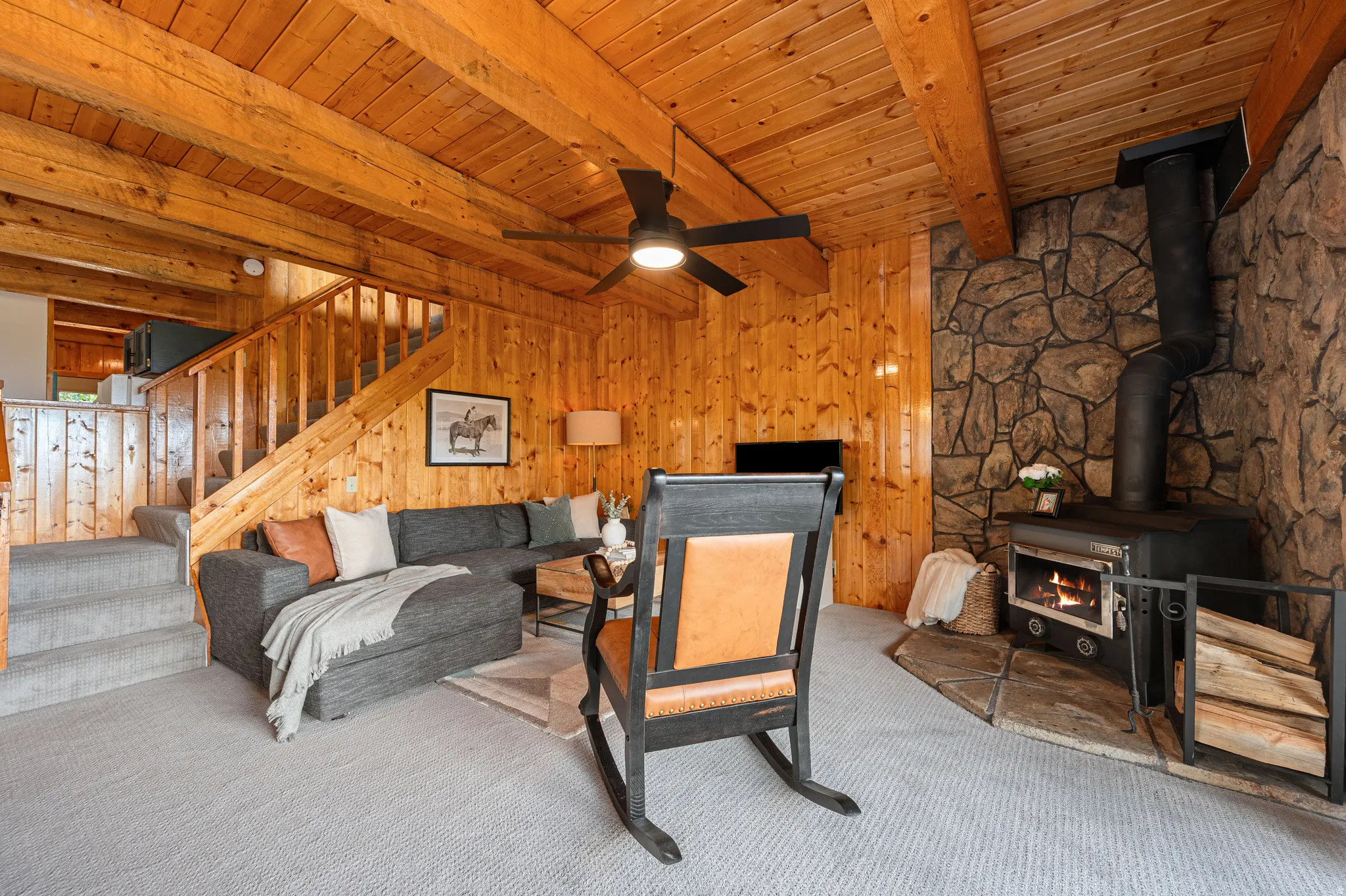 Rustic wood-beam cathedral ceiling with exposed timber framing and ceiling fan, complemented by warm knotty pine walls throughout