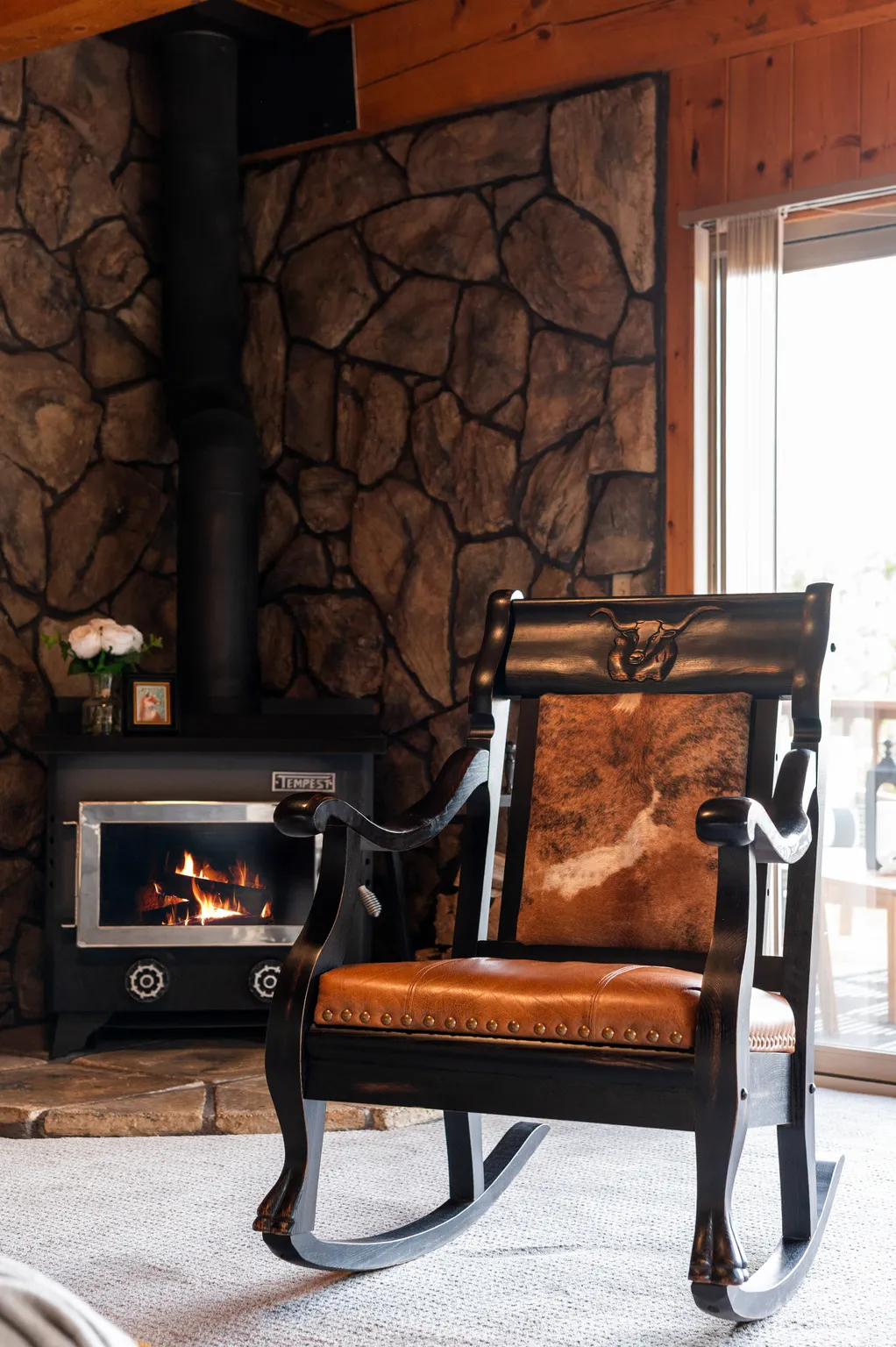 Stone accent wall, wood stove with black piping, wood ceiling, light-colored carpeting