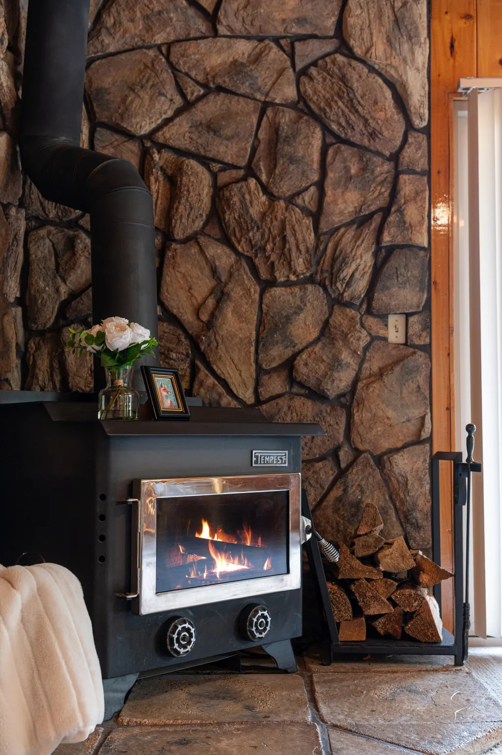 Stone-clad wall with a black wood-burning stove featuring a glass door and metal accents