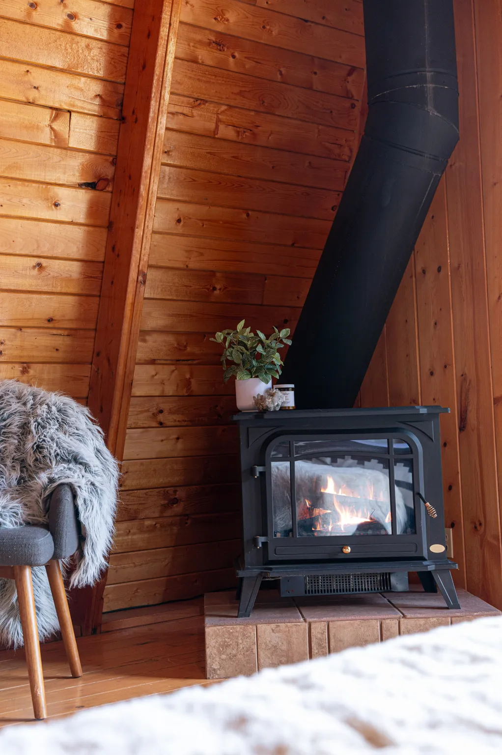 Wood-paneled wall, exposed wood beam, black wood-burning stove, tile hearth, wood-finish flooring