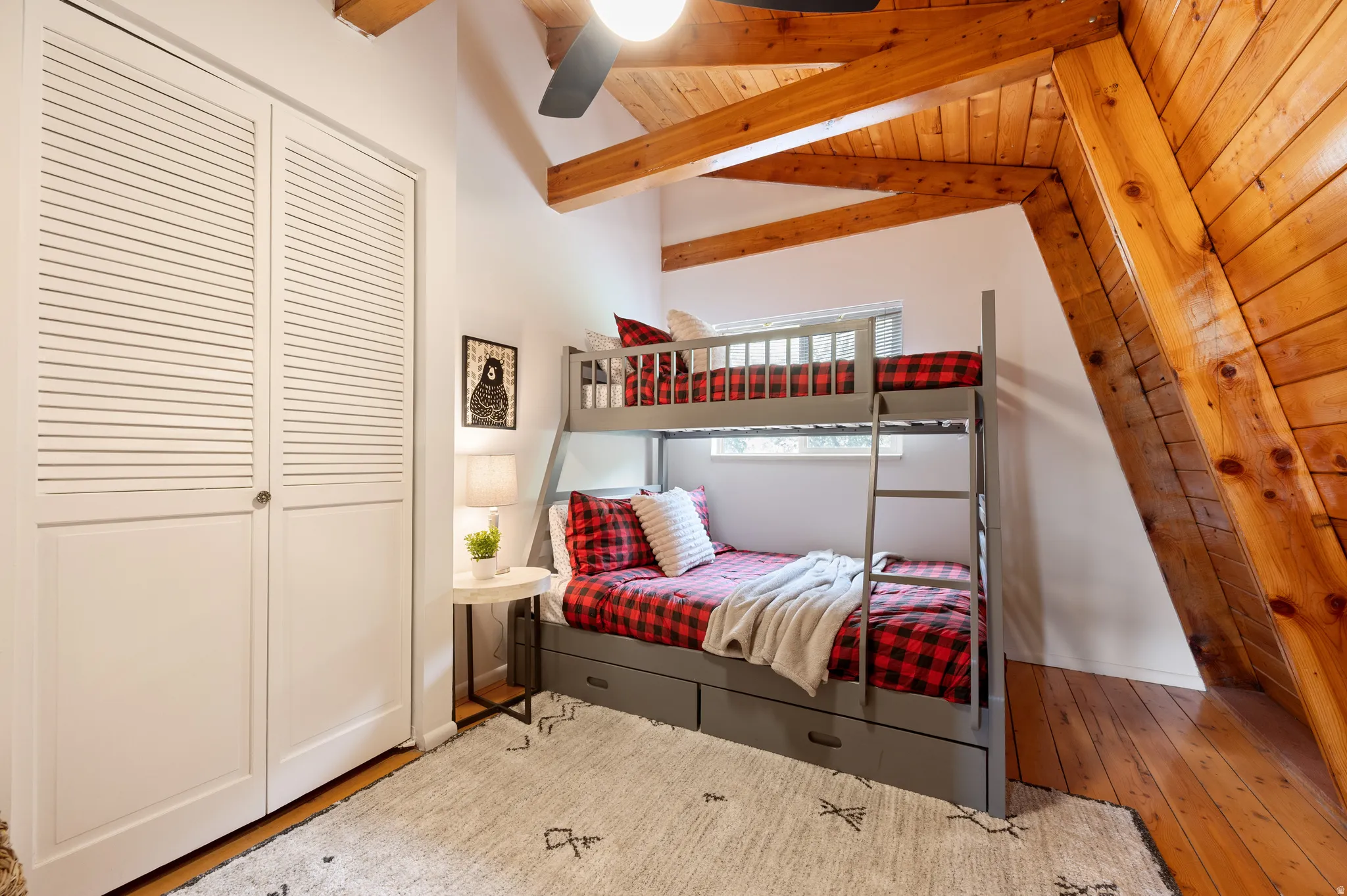 Vaulted wood-paneled ceiling with exposed beams, wood-finish flooring, white louvered bifold closet doors, and recessed window