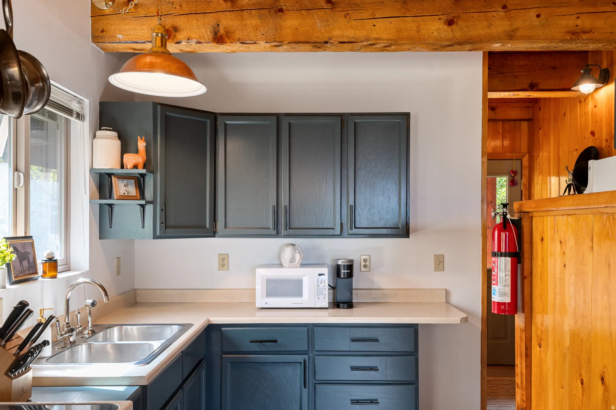 Exposed wood beams, painted cabinetry, double basin stainless steel sink, and light-toned countertops