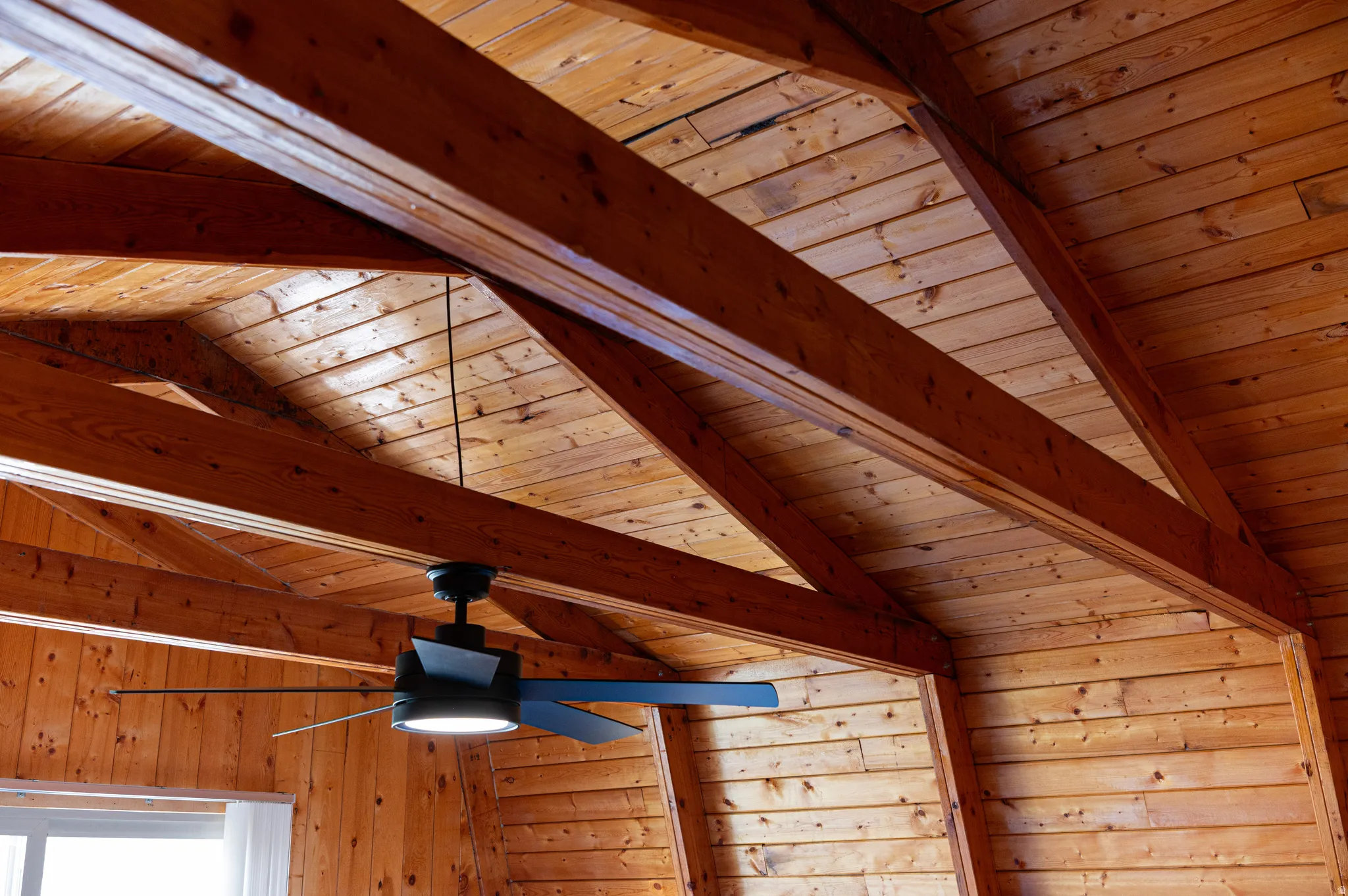 Vaulted ceiling with exposed wood beams, finished wood plank ceiling, and a modern ceiling fan with integrated lighting