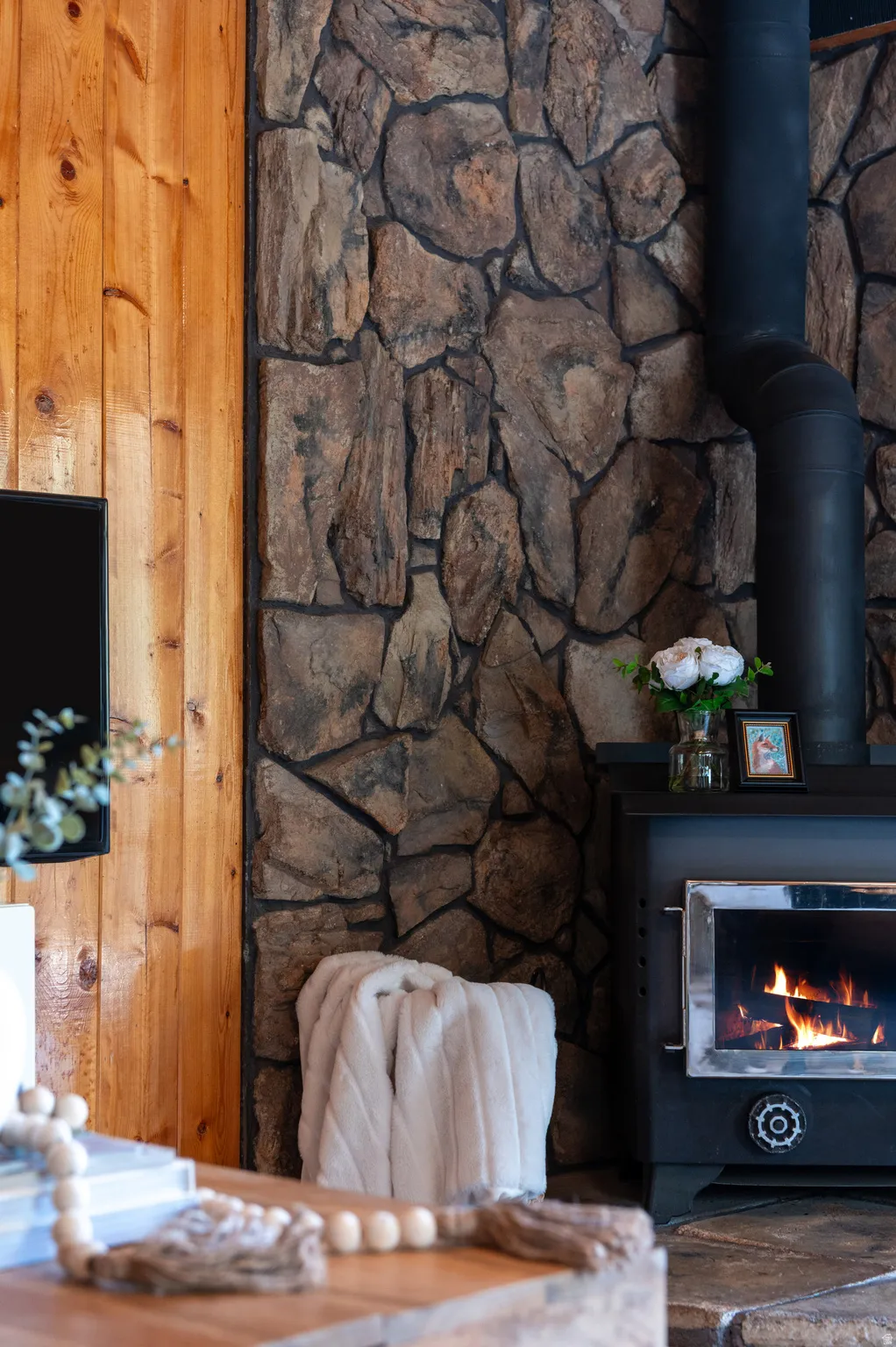 Wood-paneled wall, stone-clad accent wall, wood-burning stove, stove pipe, stone hearth