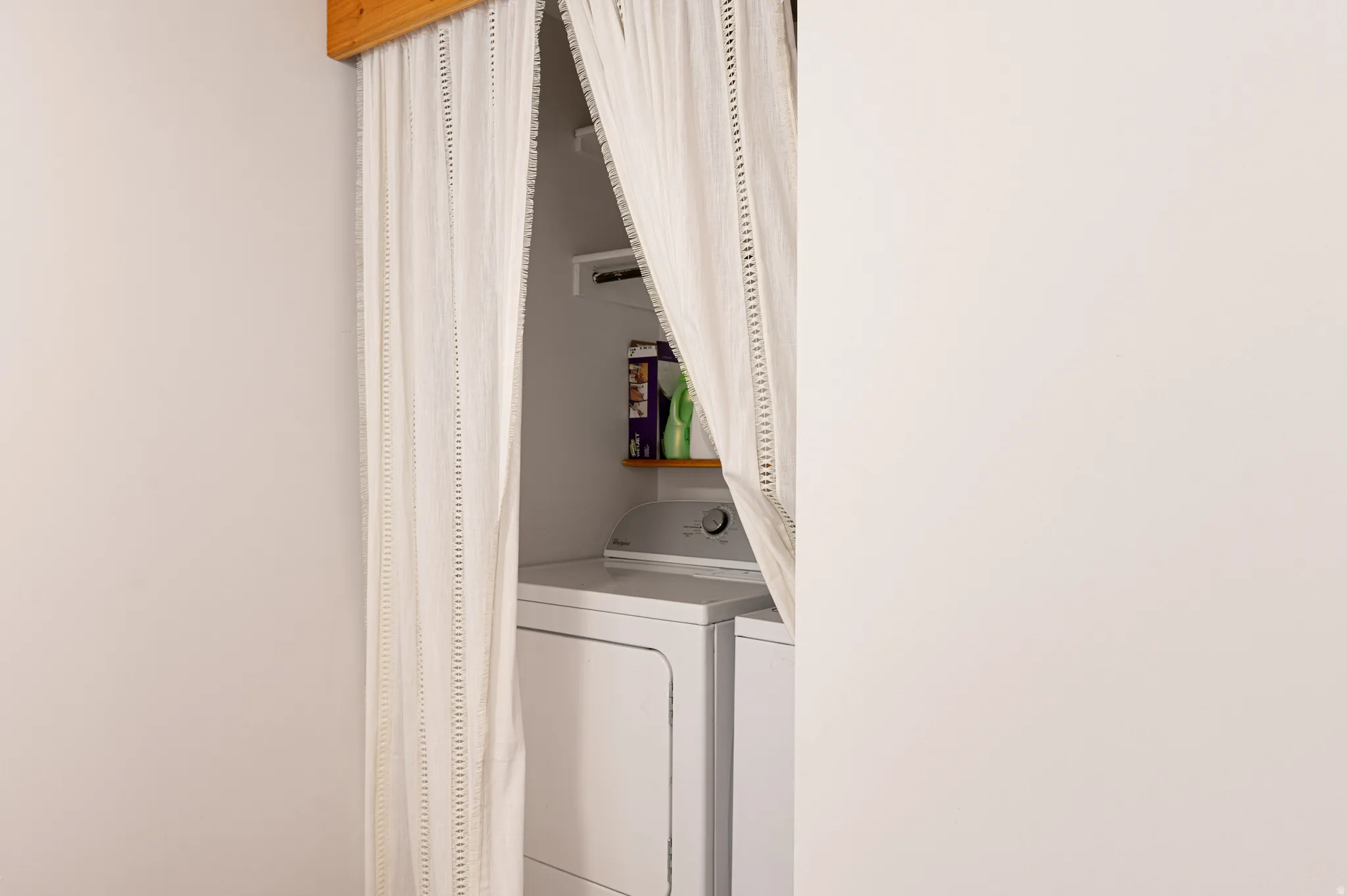 Laundry area featuring a stacked washer and dryer, wood-finish shelving, and a white curtain enclosure