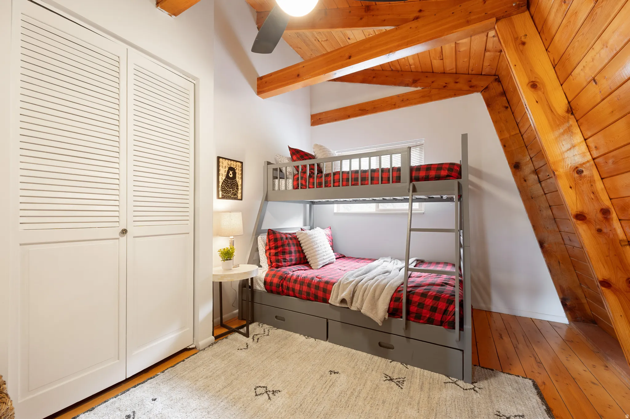 Vaulted wood-paneled ceiling with exposed beams, wood-finish flooring, white louvered closet doors, and built-in bunk beds with storage drawers