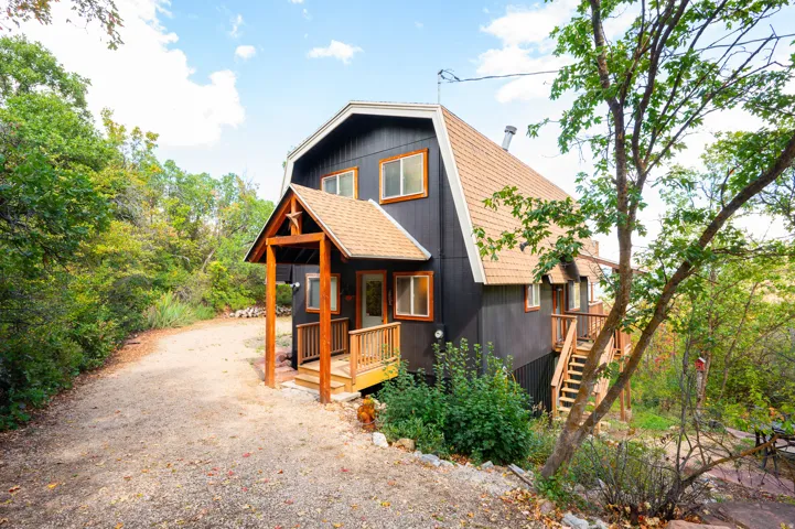 Dark-toned siding with contrasting wood trim, light-colored roofing, covered porch with wood accents, exterior staircase, and gravel driveway