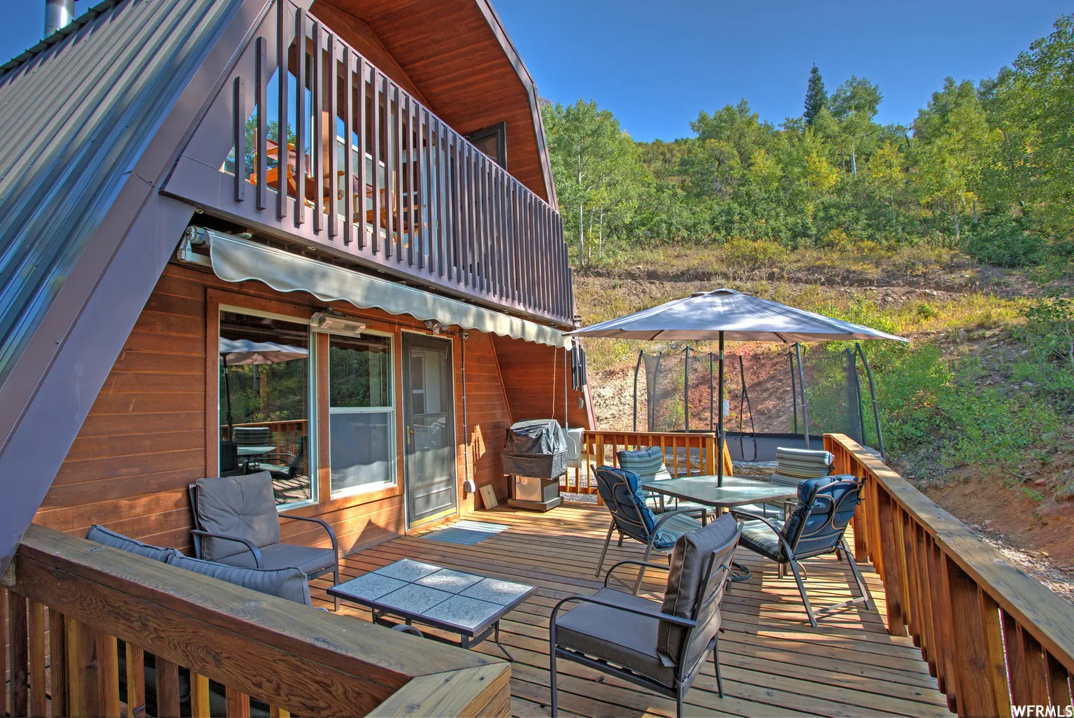 Expansive wood deck with a privacy railing, featuring a retractable awning and a second-story balcony