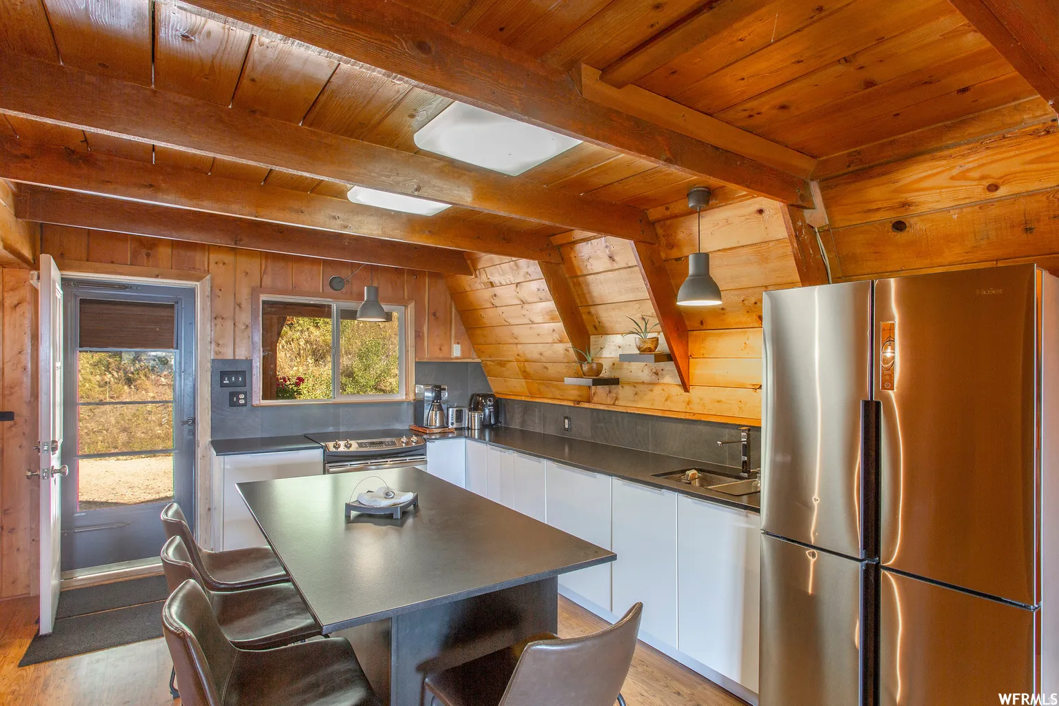 Wood-paneled ceilings with exposed beams, stainless steel refrigerator, white flat-panel cabinetry, dark countertops, and wood-finish flooring
