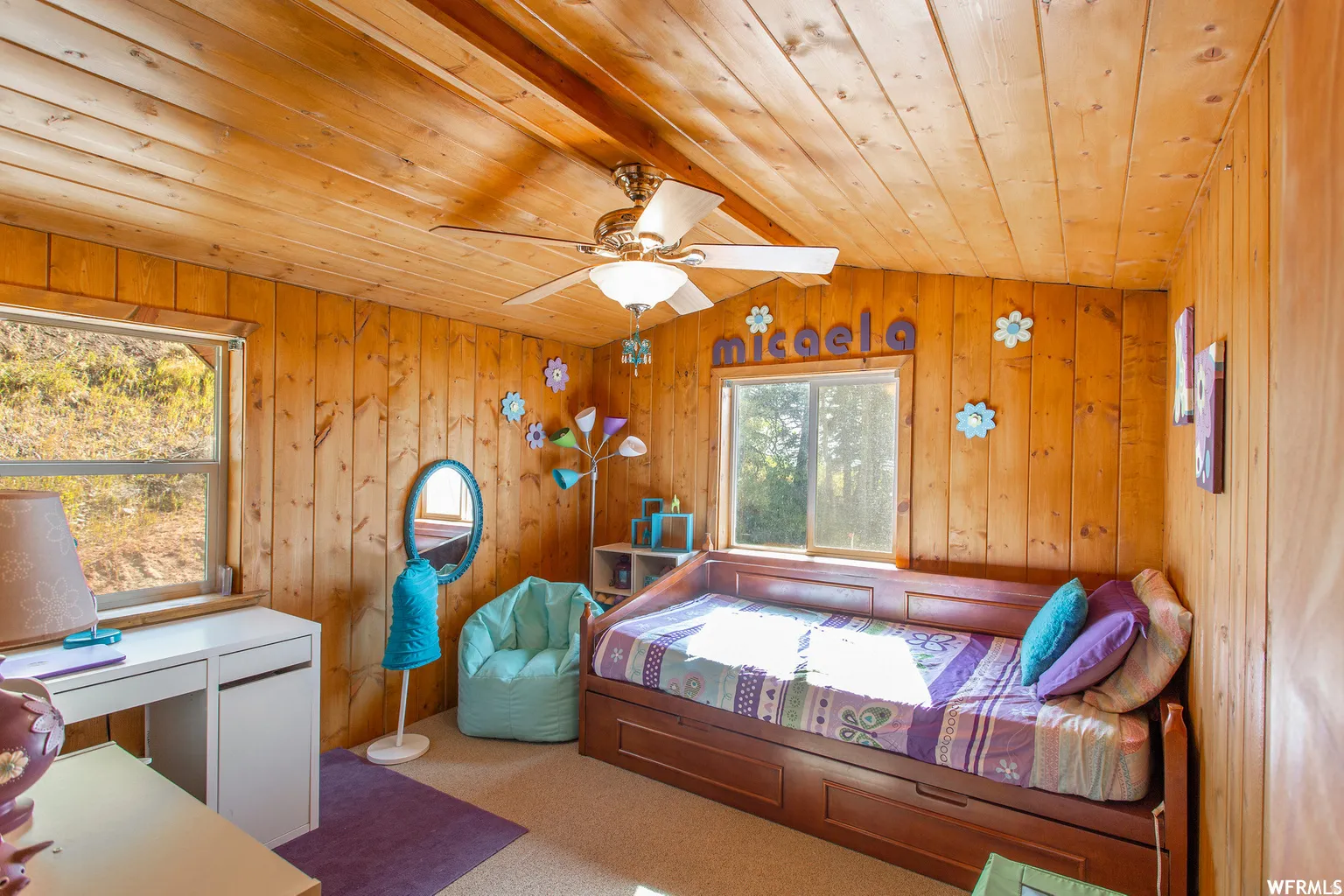 Wood-paneled walls and ceiling, two windows, carpet flooring, and a ceiling fan with integrated lighting