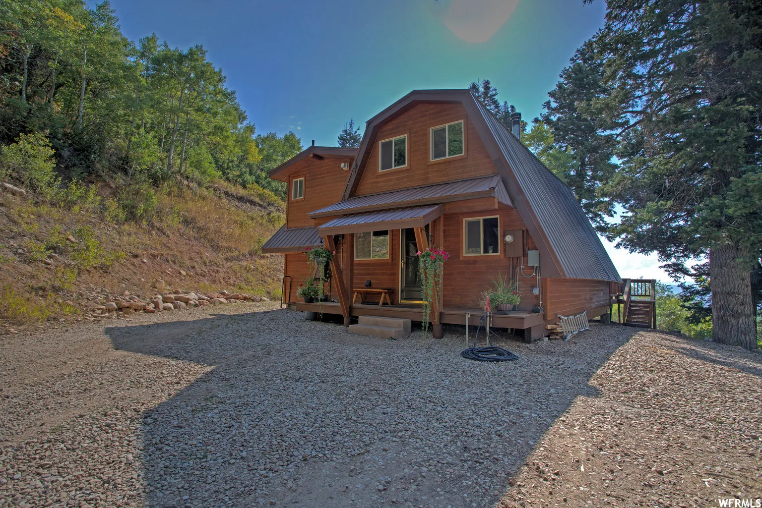 Wood-sided A-frame structure featuring a metal roof, front porch, and a gravel driveway