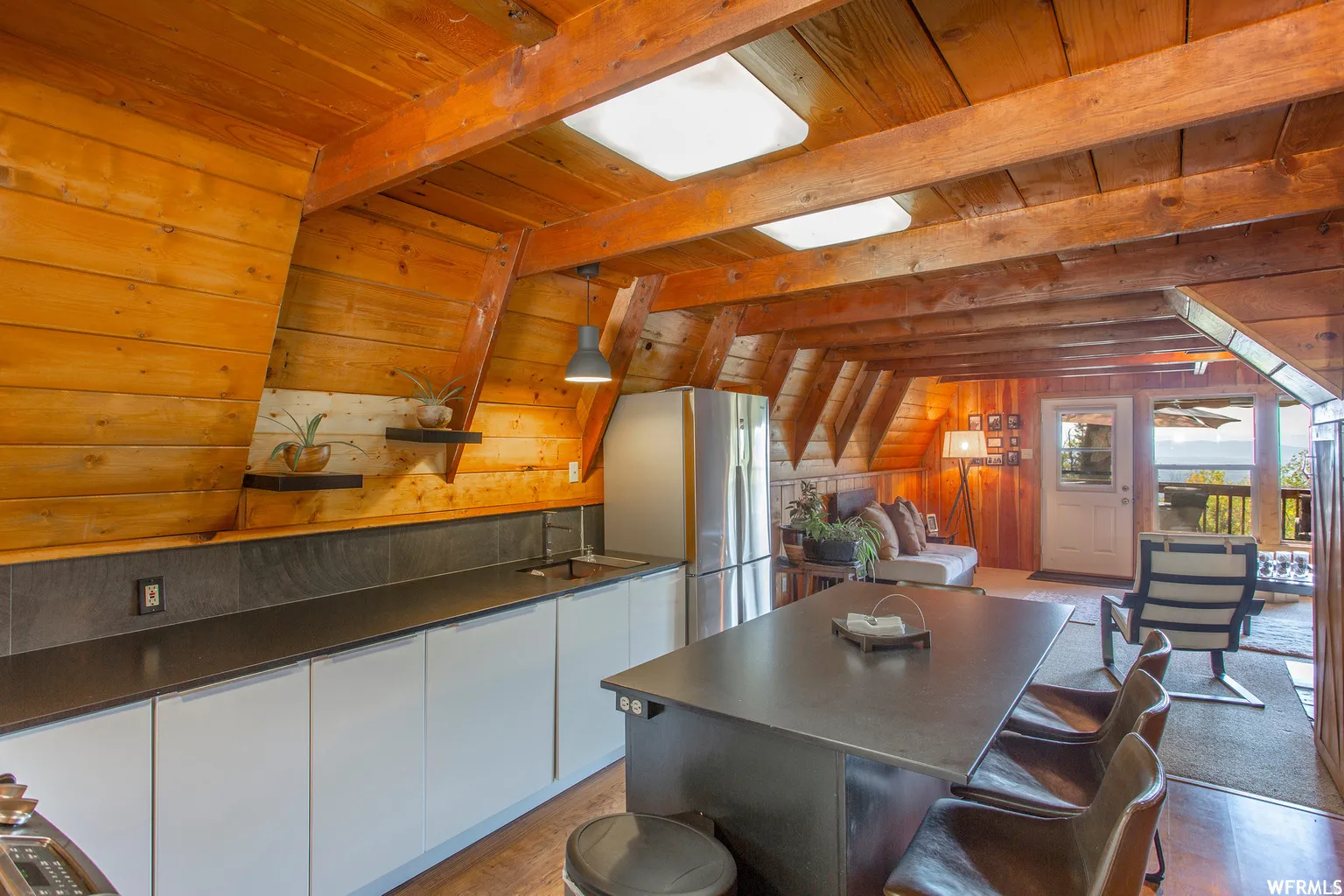 Exposed wood beams, wood-paneled walls, sleek flat-panel cabinetry, a stainless steel refrigerator, and a built-in island