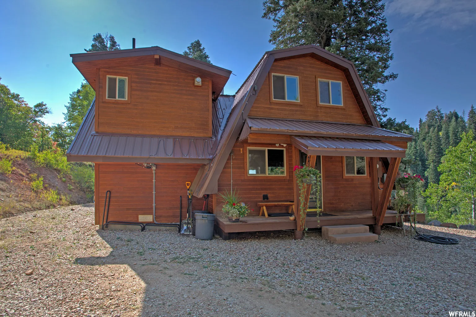 Wood-sided dwelling with a brown metal roof, featuring multiple windows and an inviting covered porch