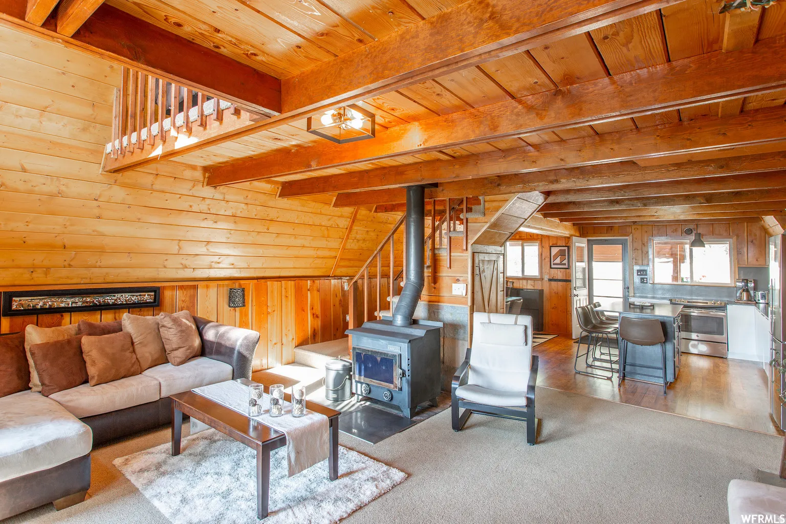 Wood-paneled interior featuring exposed ceiling beams and a central wood-burning stove