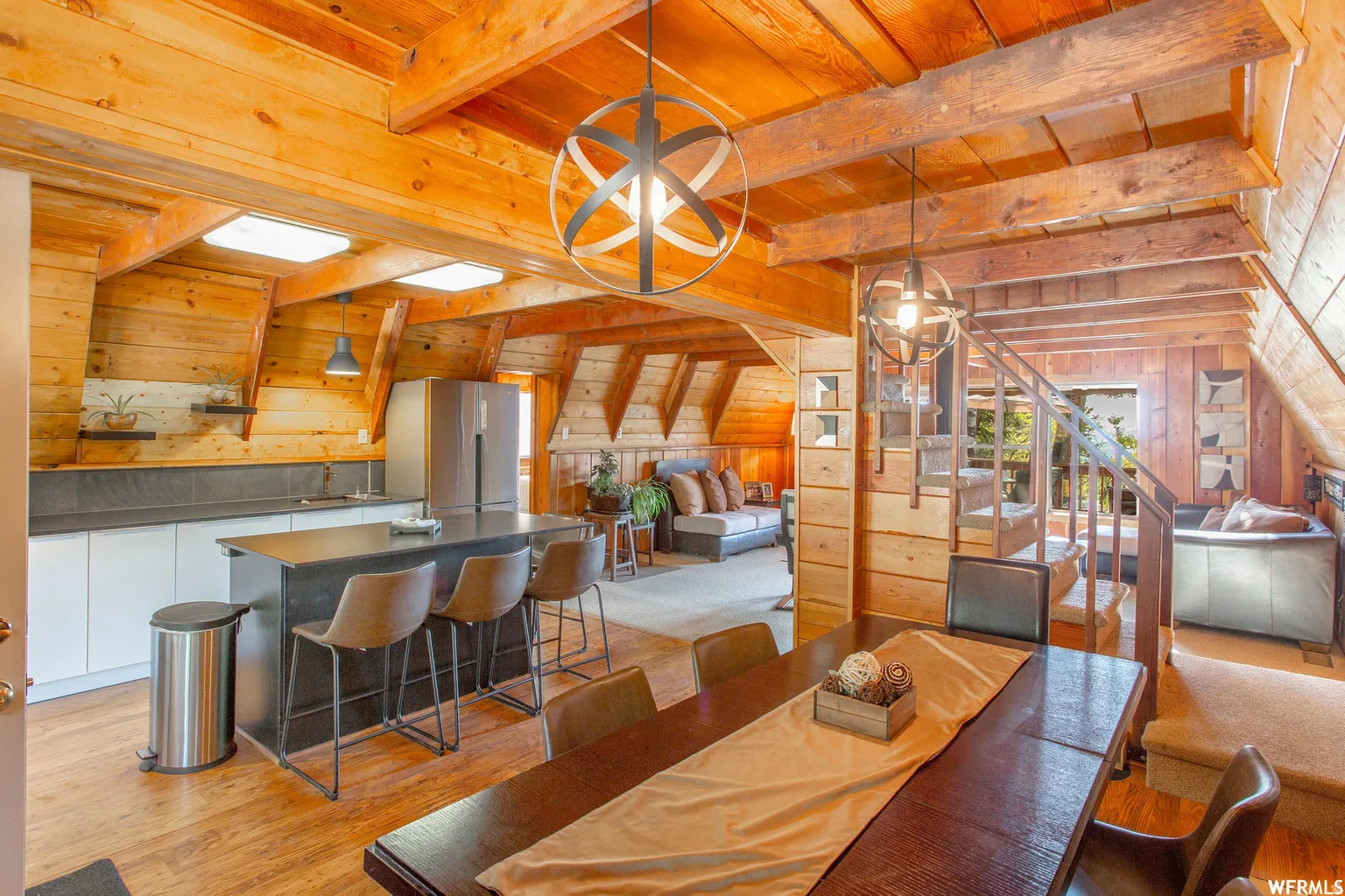 Wood-paneled ceilings with exposed beams, kitchen island with counter seating, built-in staircase, and modern spherical light fixtures