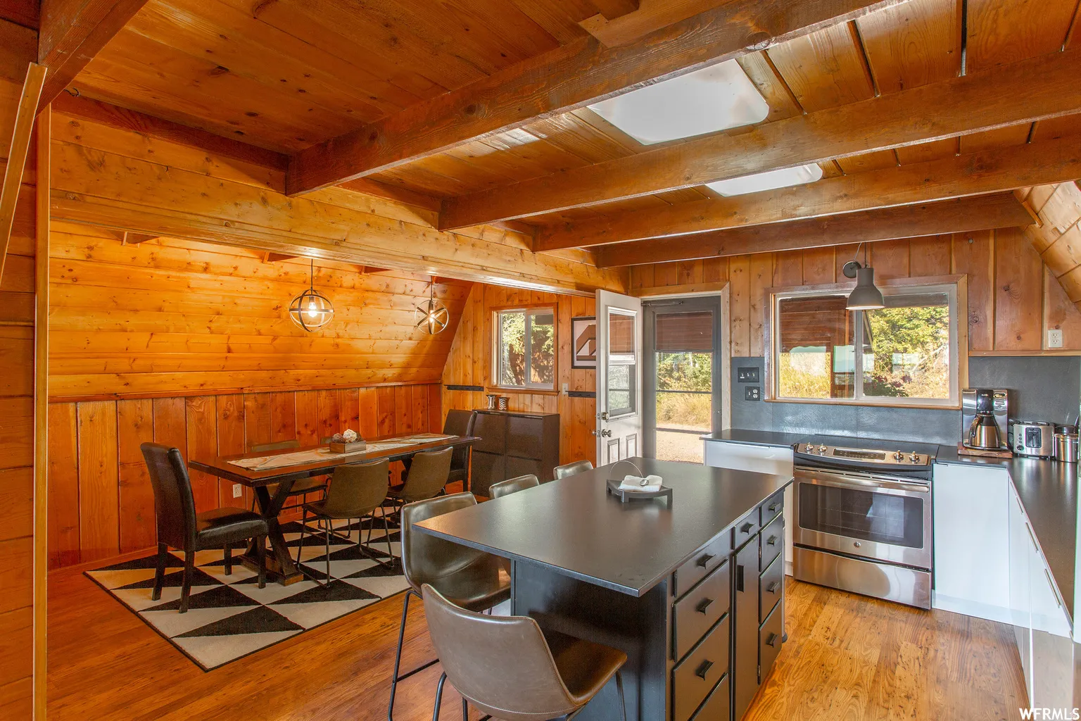 Wood-paneled walls and ceiling beams, open-concept kitchen with a center island, stainless steel range, and skylights