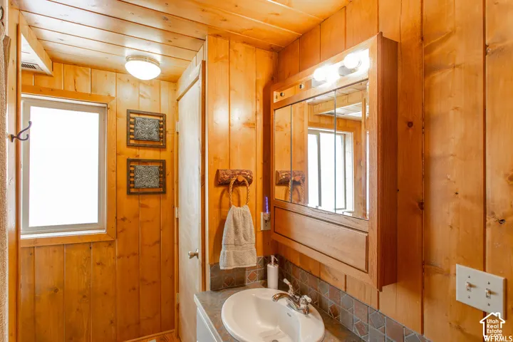 Wood-paneled walls and ceiling, built-in medicine cabinet with integrated lighting, window for natural light, and a vanity with an integrated sink