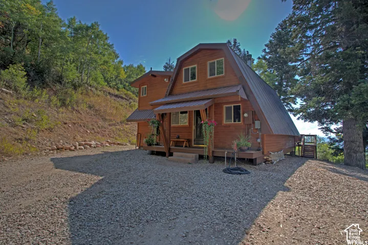 Wood-sided A-frame structure featuring a metal roof, front porch, and a gravel driveway