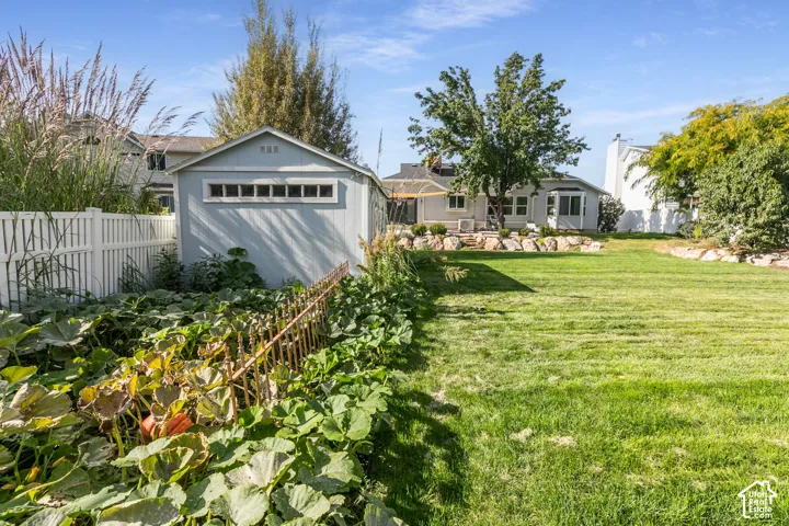 Expansive lawn area with a dedicated garden plot, white picket fencing, and a detached storage shed