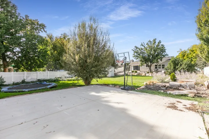 Expansive concrete patio, manicured lawn, white privacy fence, mature trees, landscaped rock features