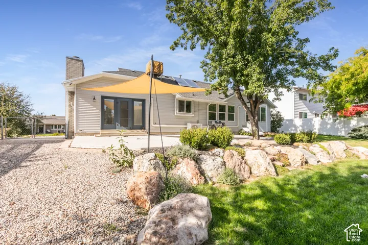 Rear exterior featuring light-toned siding, a brick chimney, and a multi-pane glass door opening to a concrete patio