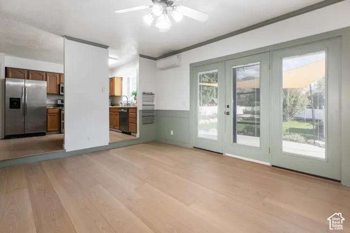 Light wood-finish flooring with a ceiling fan, French doors, and a kitchen featuring wood cabinetry and stainless steel appliances