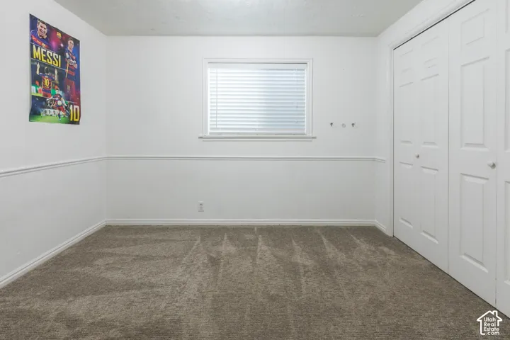Neutral-toned carpet flooring, white walls with chair rail molding, a white-framed window with horizontal blinds, and bi-fold closet doors