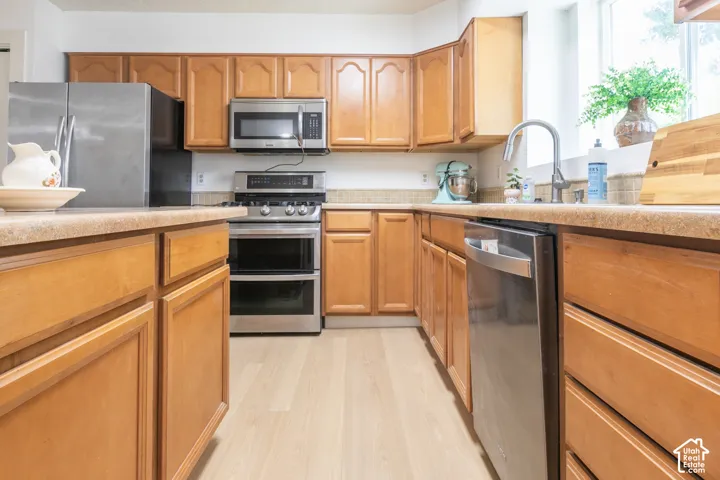 Kitchen featuring light wood-finish cabinetry, stainless steel appliances, light-colored countertops, and light wood-finish flooring