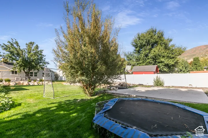 Expansive backyard featuring a green lawn, mature trees, a concrete pad, and a white fence