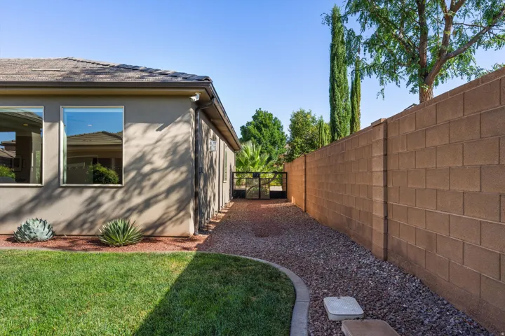 Manicured lawn, mature landscaping, stucco exterior, block wall, and a side gate