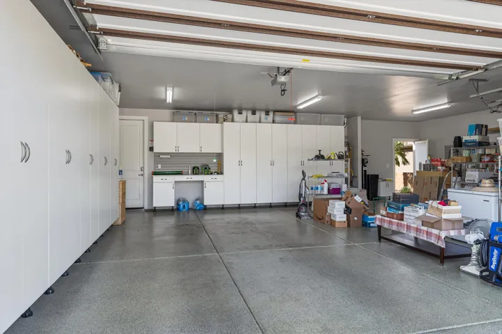 Garage with extensive white cabinetry, speckled concrete flooring, recessed lighting, and an additional white entry door