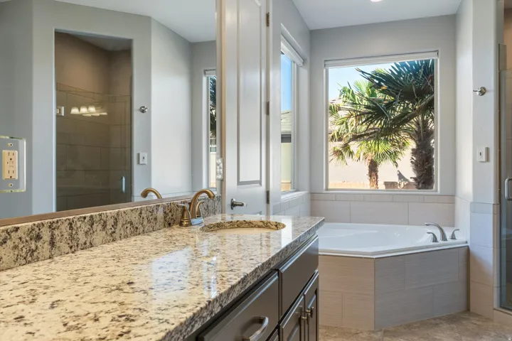 Dual sink vanity with granite countertop, built-in soaking tub, and tile-surround shower with glass enclosure