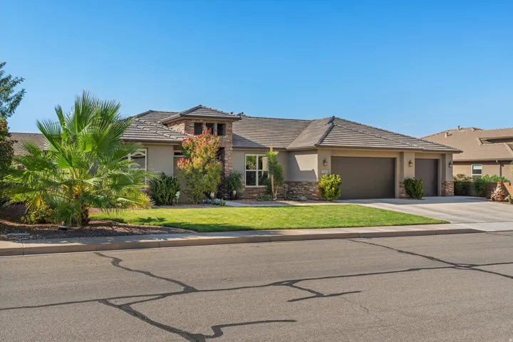 Stucco exterior with stone accents, tile roof, attached multi-car garage, and a manicured lawn